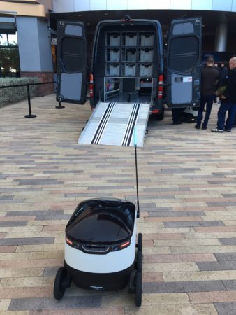 A robot from Starship Technologies prepares to grab a package from a Sprinter van.