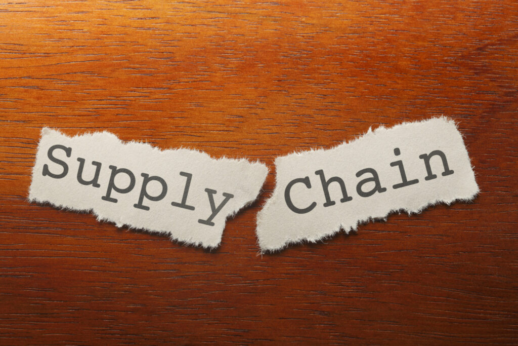 "Supply Chain" printed on a piece of paper that is torn into two pieces resting on a wood desk.