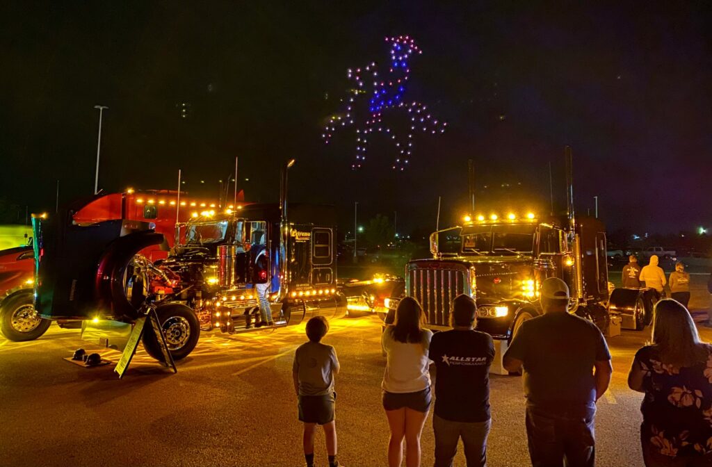 People watch a drone show with trucks parked