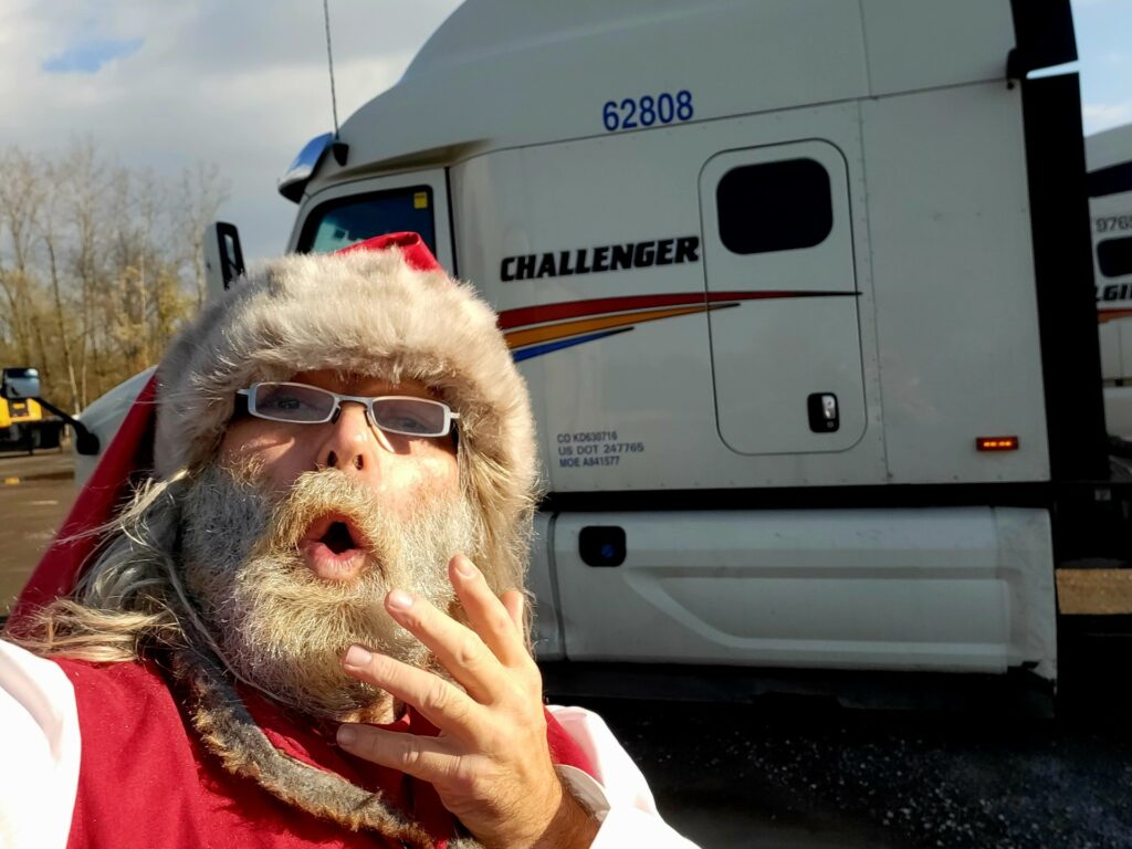 The photo is a selfie of Dave Bennison, a truck driver, dressed as Santa Clause in front of a Challenger truck