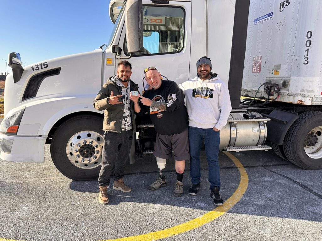 Picture of Chris Miners in front of a truck with two driving school owners