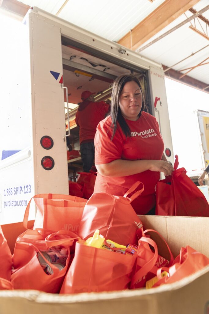 The image is of a women, a team member of Purolator Tackle Hunger, delivering food to the food bank