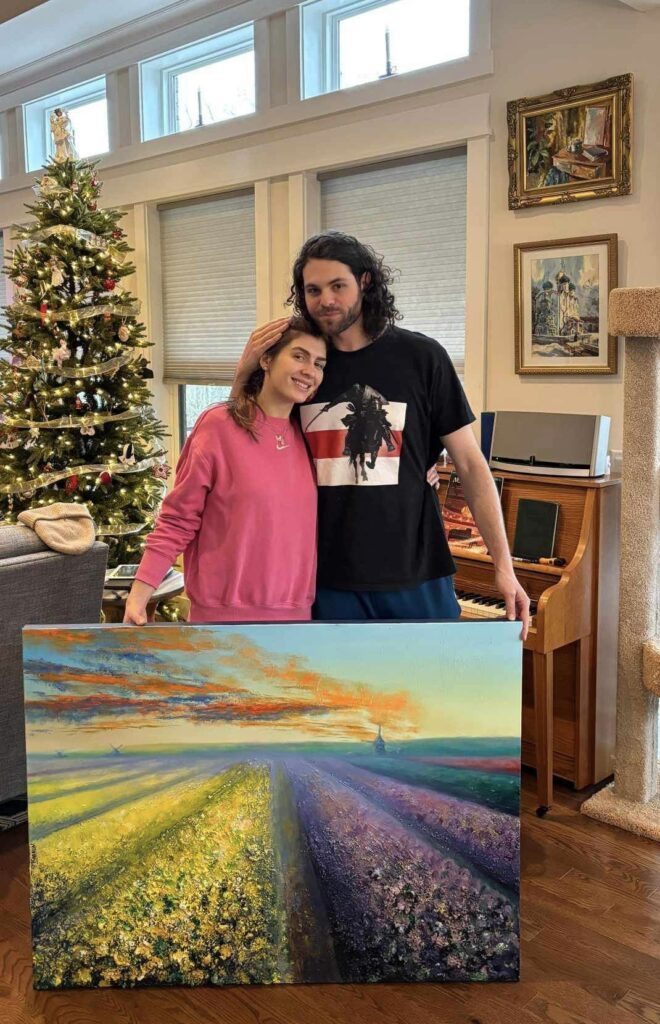 The image is of the couple at home holding Eugene Kabrun's painting, Flower Farm