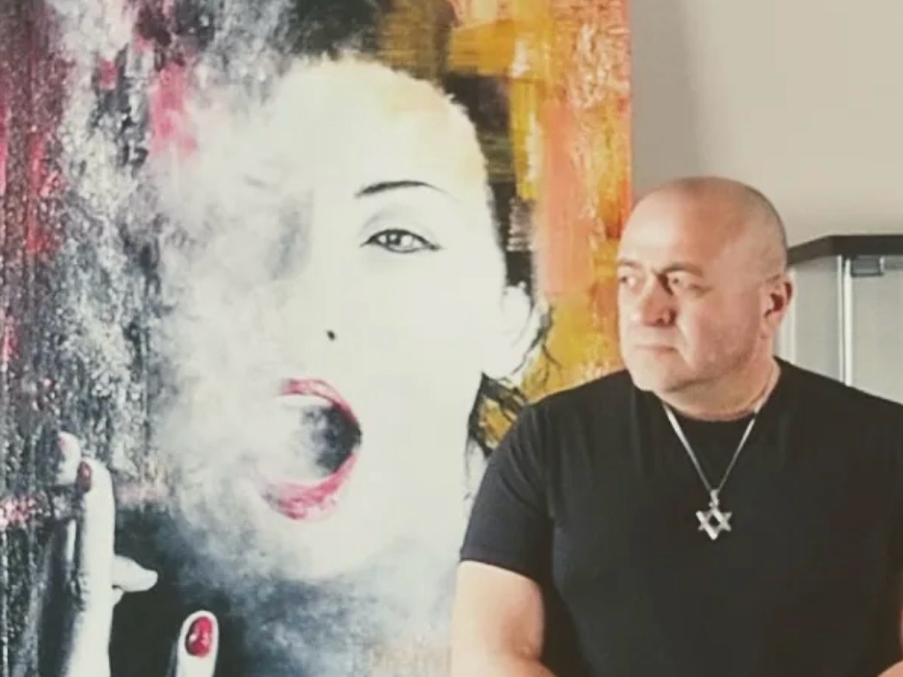 This is a headshot of Eugene Kabrun standing in front of his painting called Passionate Smoker
